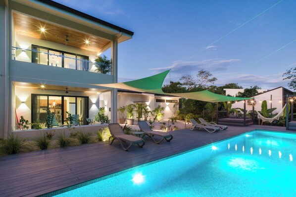 Une maison moderne à deux étages, dotée d’une piscine, de chaises longues et d’un hamac.