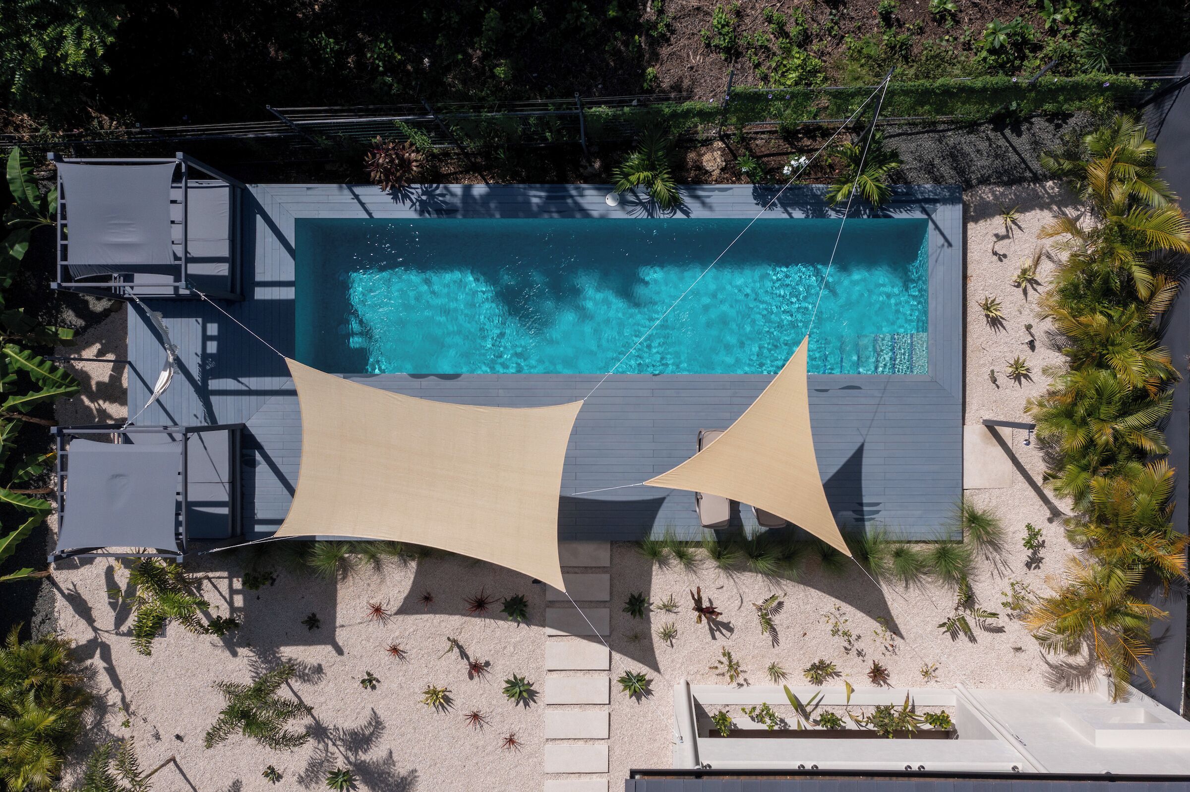 A rooftop pool with clear blue water, surrounded by a sandy area with plants and a shaded structure.