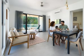 Een moderne woonkamer met een bank, een eettafel en stoelen. Er is een balkon met buitenmeubilair.