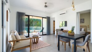 Un salon moderne avec un canapé, une table à manger et des chaises. Il y a un balcon avec vue sur la verdure.