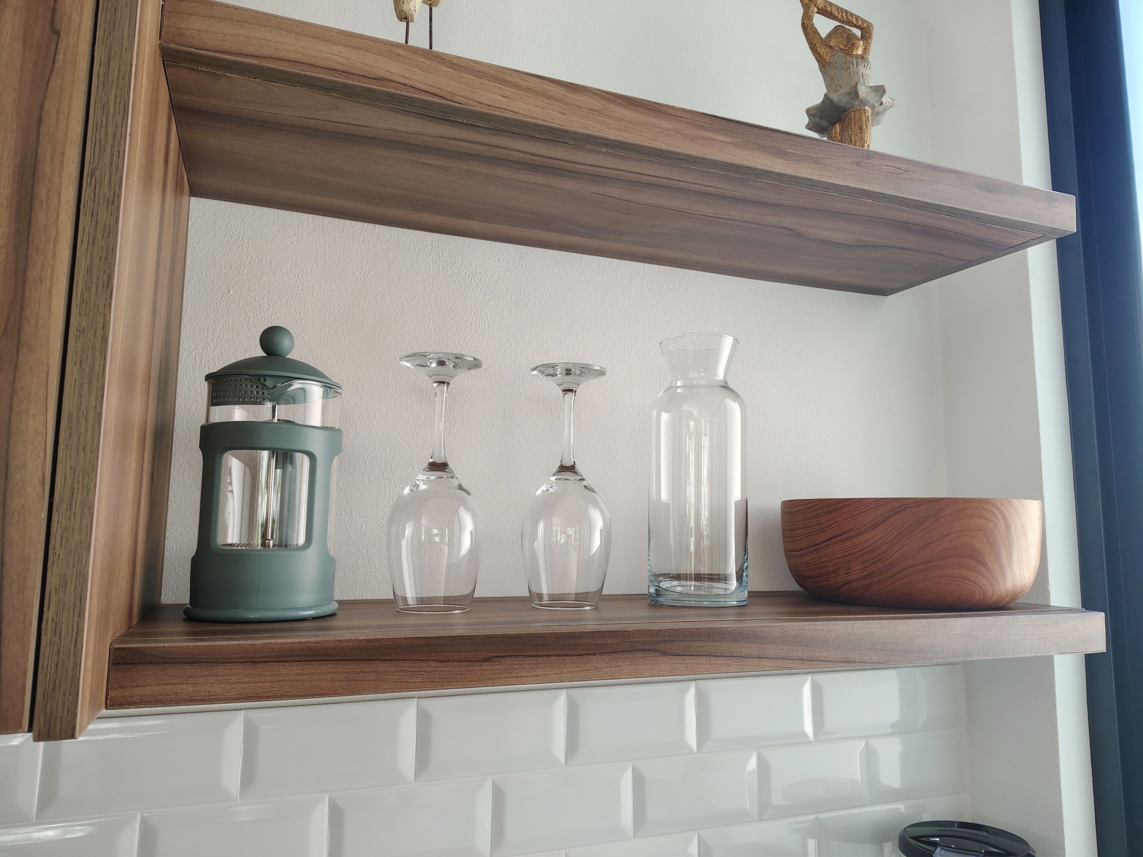 A wooden shelf with a green lantern, three wine glasses, and a clear bottle.
