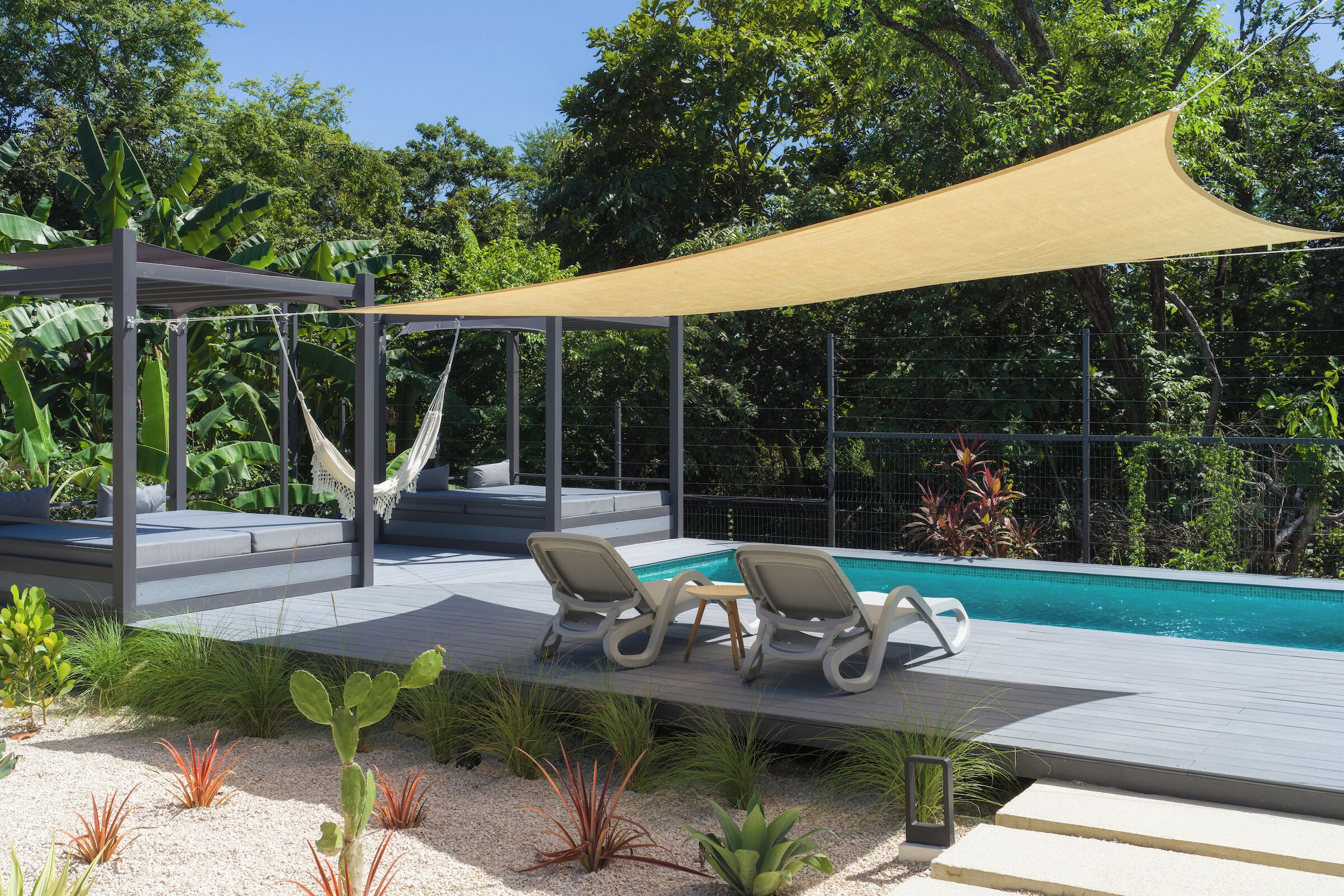 A poolside area with a canopy, lounge chairs, and a hammock.