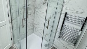 A glass-enclosed shower with a curved ceiling, marble tiles, and a metal towel rack.