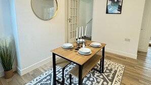 A dining area with a wooden table set for four, a mirror, and a framed artwork on the wall.