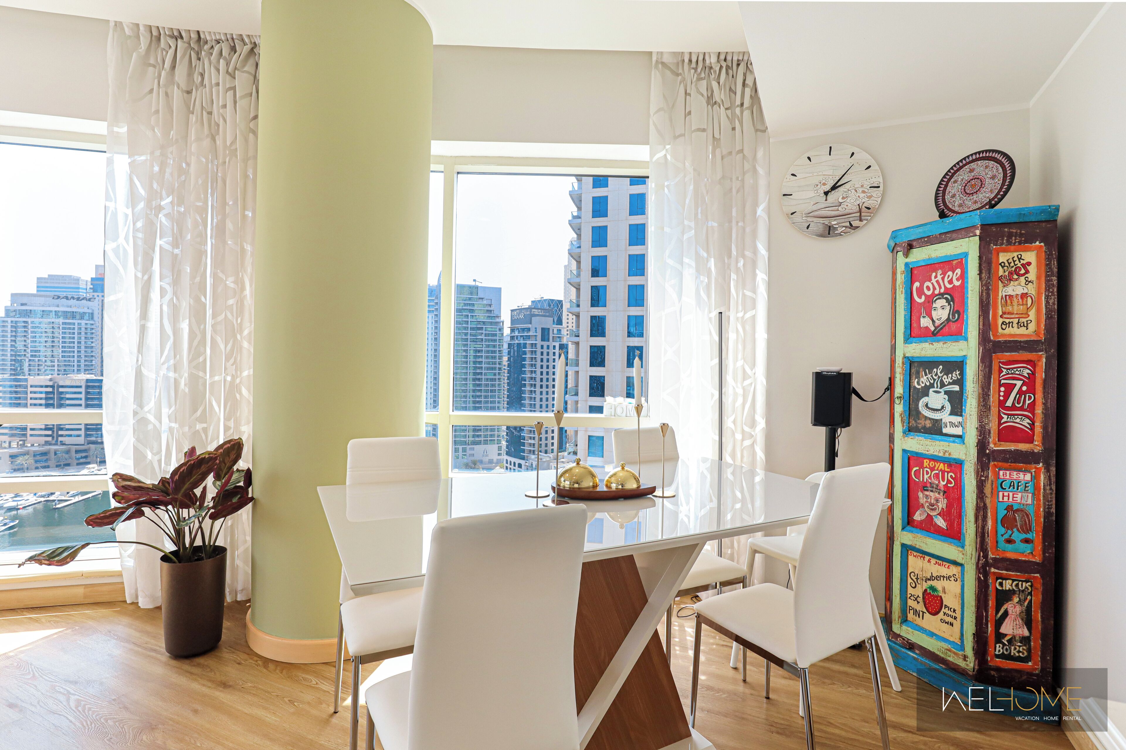 A modern dining area with a glass table, white chairs, a potted plant, and a decorative wall panel.