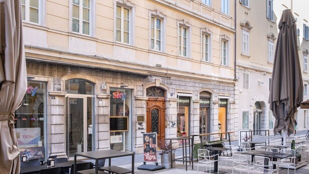 An outdoor cafe with tables and chairs, a wooden door, and a building with multiple windows and awnings. - The Architect - Exclusive Loft in Ponteroso (Trieste)