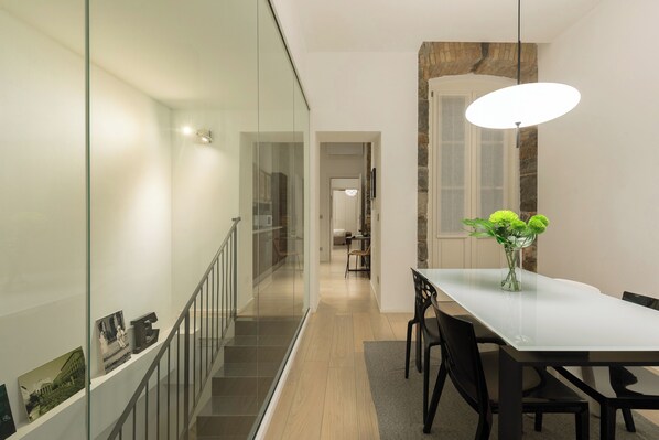 A modern dining area with a glass partition, a staircase, and a dining table with chairs.