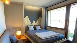 A bedroom with a bed, bedside table, lamp, and a window with a view.
