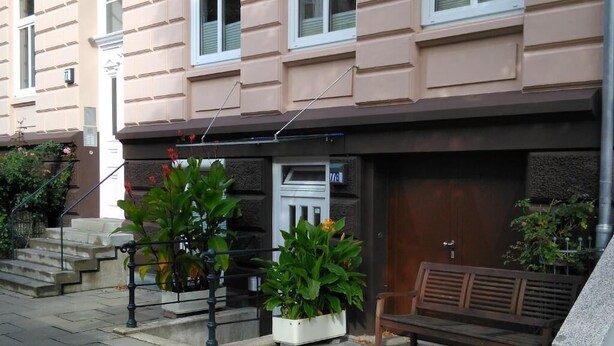 A building with a beige facade, a wooden bench, and potted plants. - Darz Gästezimmer (Hamburg)