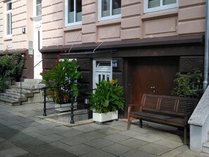 Un edificio con fachada color beige, un banco de madera y plantas en macetas.