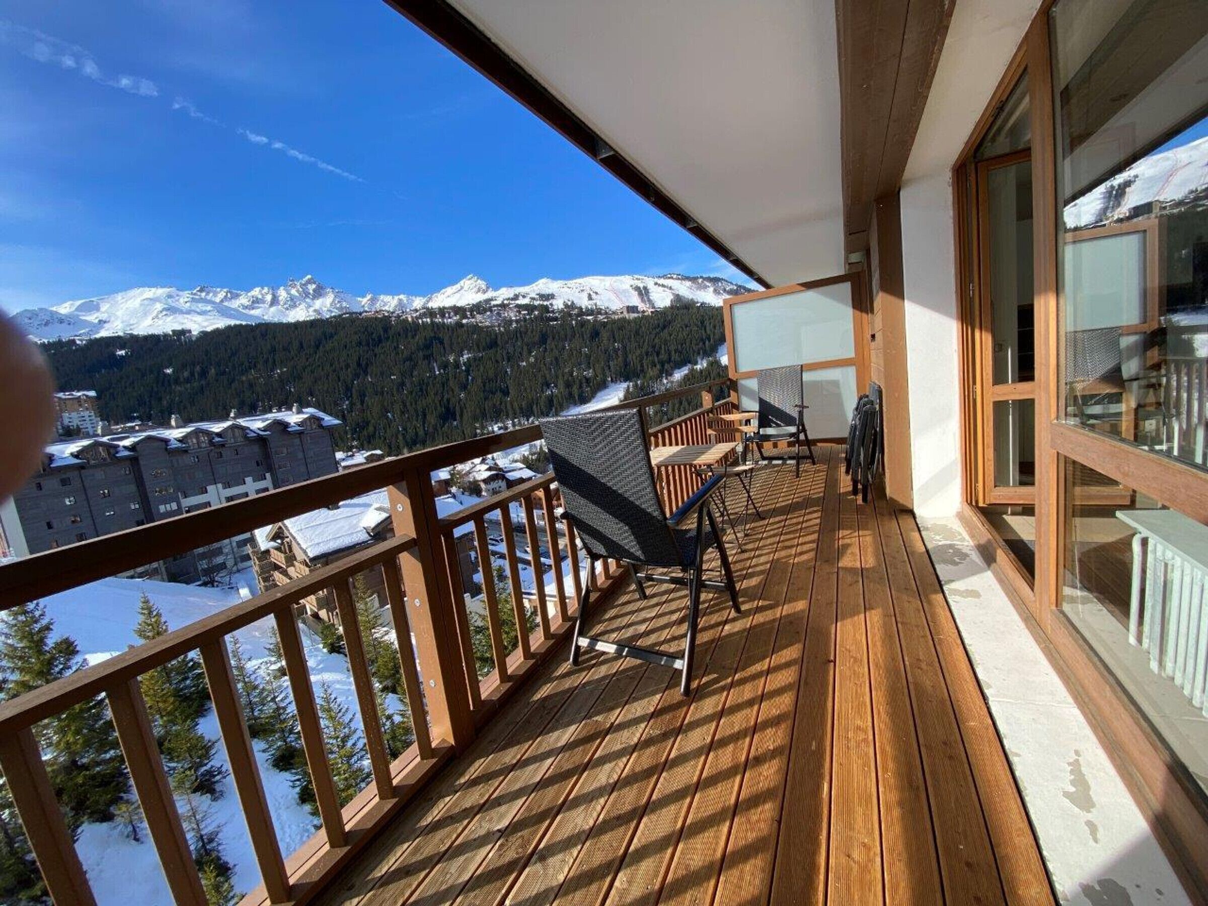 A wooden deck with a view of snow-covered mountains and pine trees.