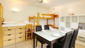 Une chambre avec un lit superposé, une table à manger pour deux personnes, une chaise et une étagère sur laquelle est posé un ours en peluche.