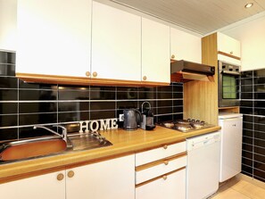 Eine moderne Küche mit weißen Schränken, schwarzer Spritzschutzwand, Spüle aus Edelstahl, Arbeitsplatte aus Holz und einem eingebauten Ofen.