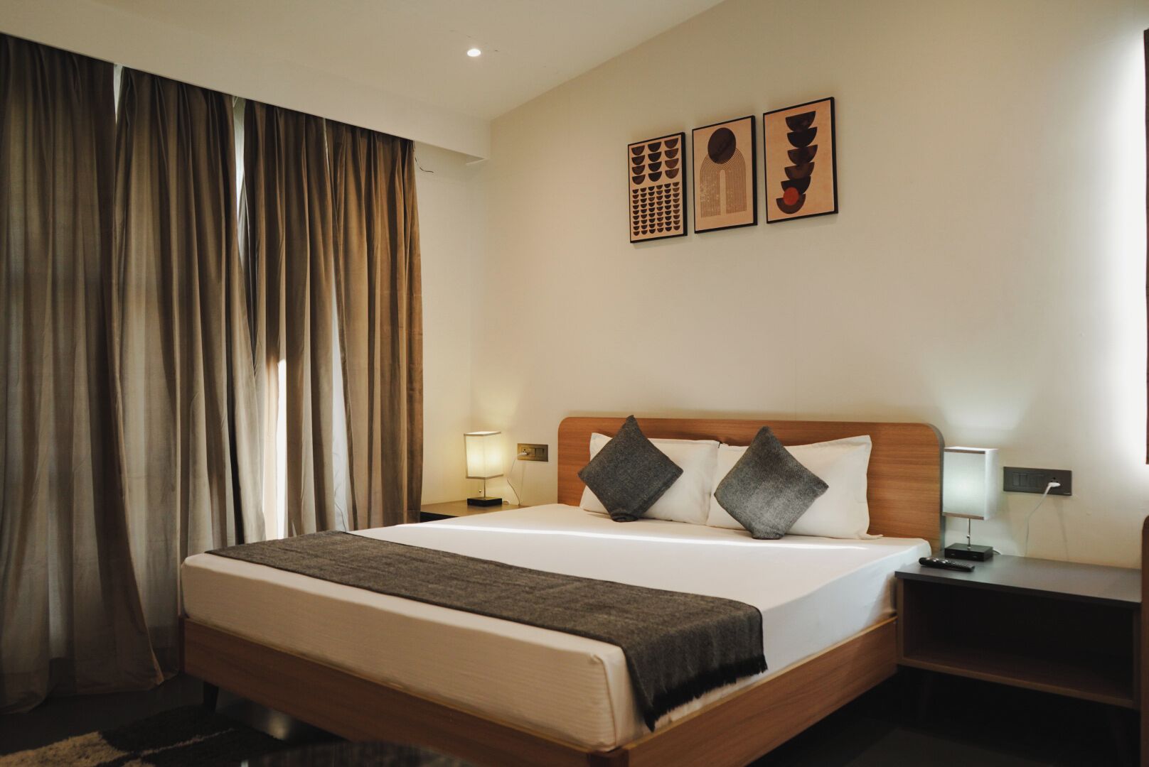 A hotel room with a large bed, two bedside tables, a nightstand, and a wall with three framed artworks.