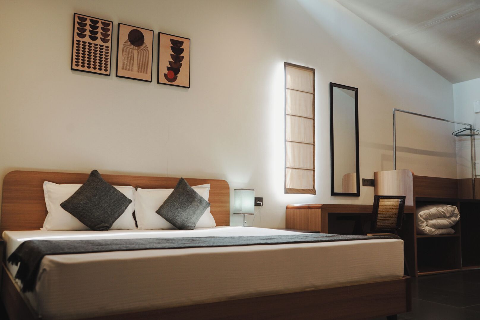 A hotel room with a large bed, a bedside table, a mirror, and a wardrobe.