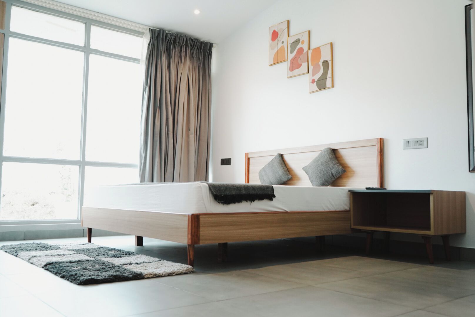 Ein modernes Schlafzimmer mit einem hölzernen Bett, einem Nachttisch und einem großen Fenster mit Vorhängen.