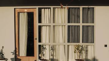 Ein Haus mit Holztür, großen Fenstern mit Vorhängen und Blumentöpfen auf der Veranda.