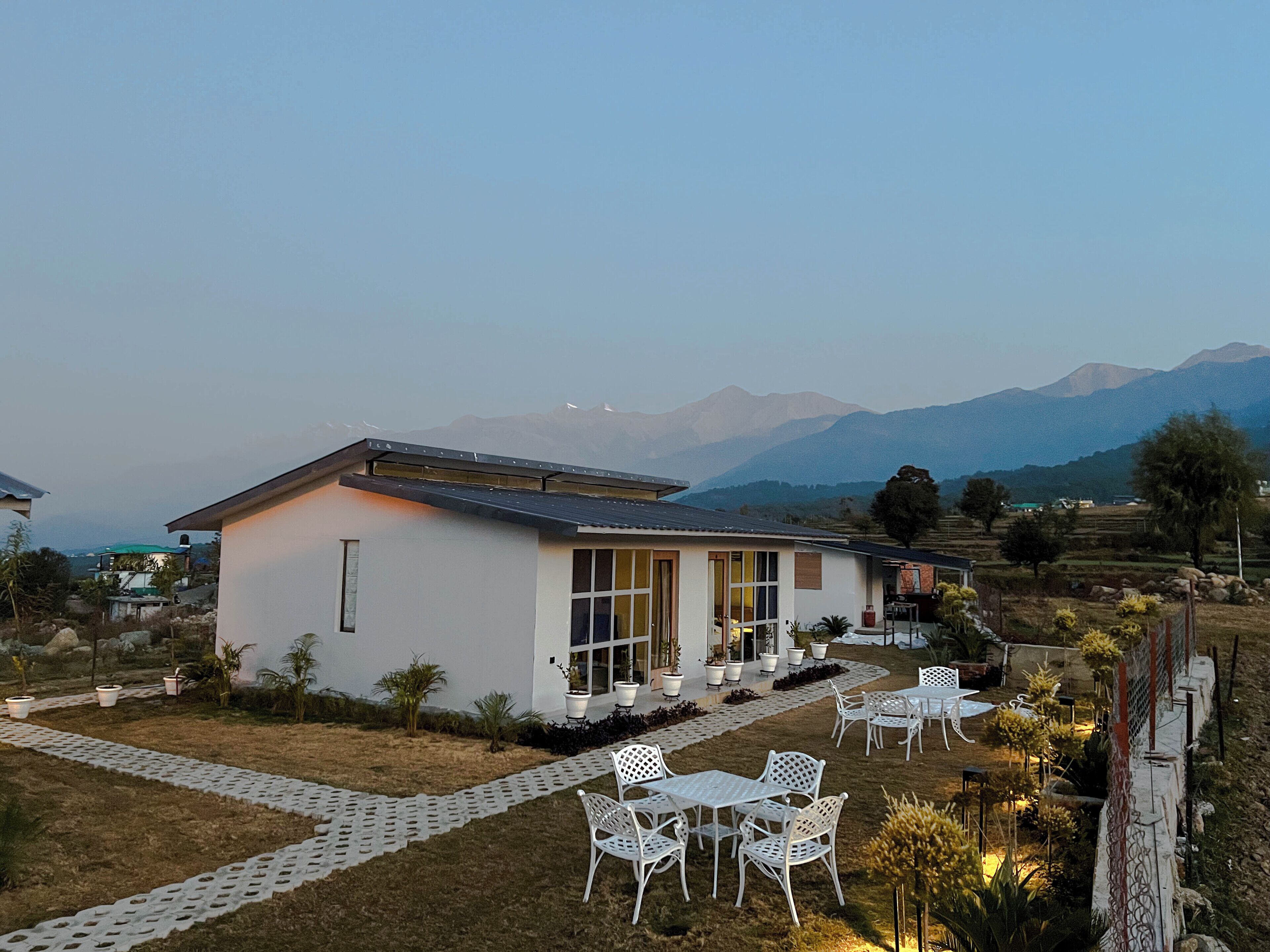 Une maison moderne dotée d’un patio, de meubles d’extérieur blancs et offrant une vue sur les montagnes en arrière-plan.