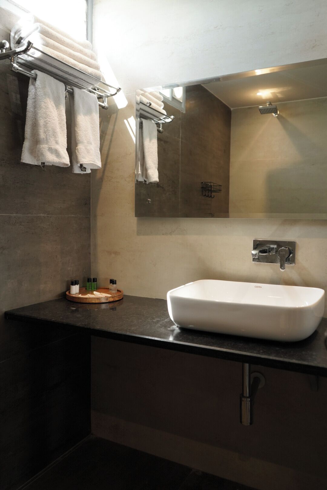 Un baño moderno con un lavamanos blanco, encimera oscura y varias toallas en un perchero.