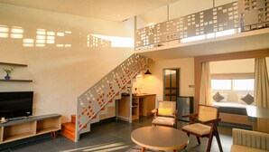 A modern living room with a staircase, a flat-screen TV, seating area, and a kitchen.