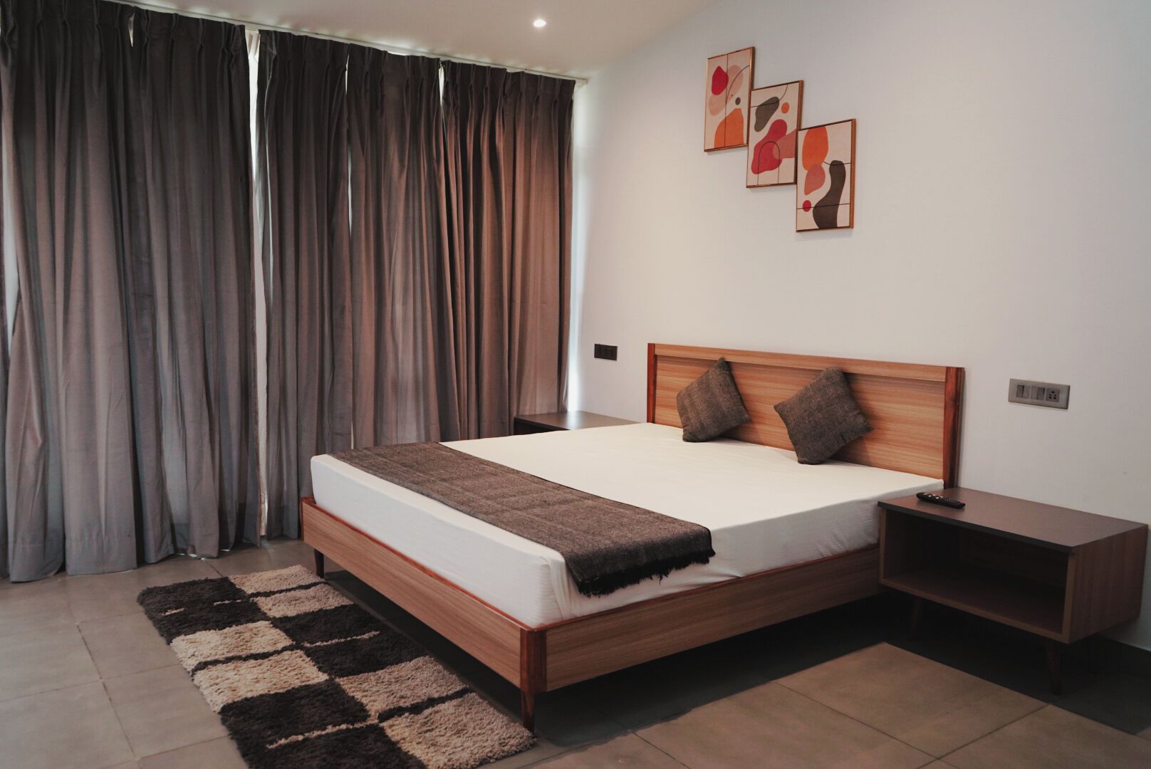 A modern bedroom with a wooden bed, a nightstand, and a large window with curtains.