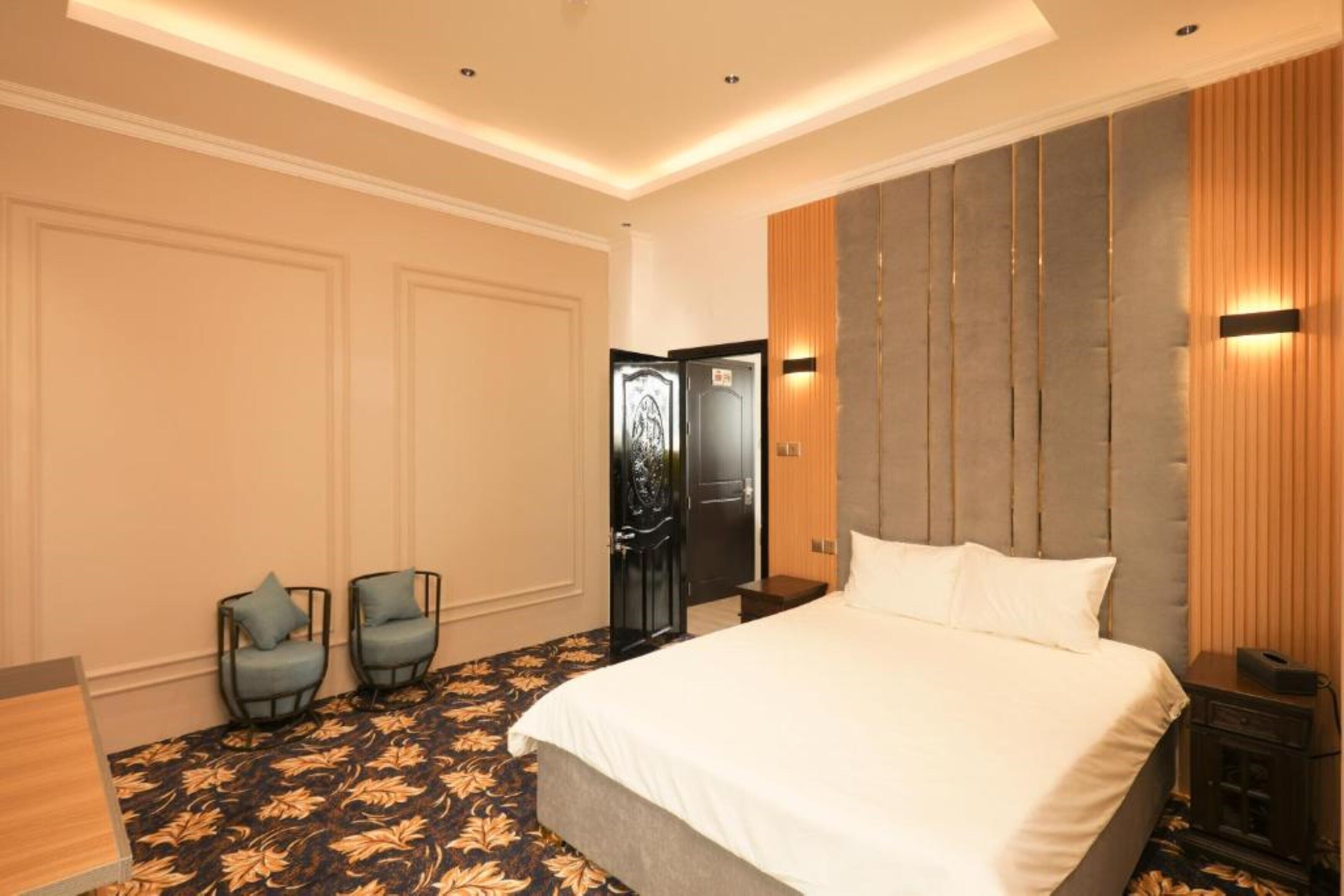 Une chambre d’hôtel avec un grand lit, deux fauteuils, un plancher en bois et une porte dotée d’un cadre noir.
