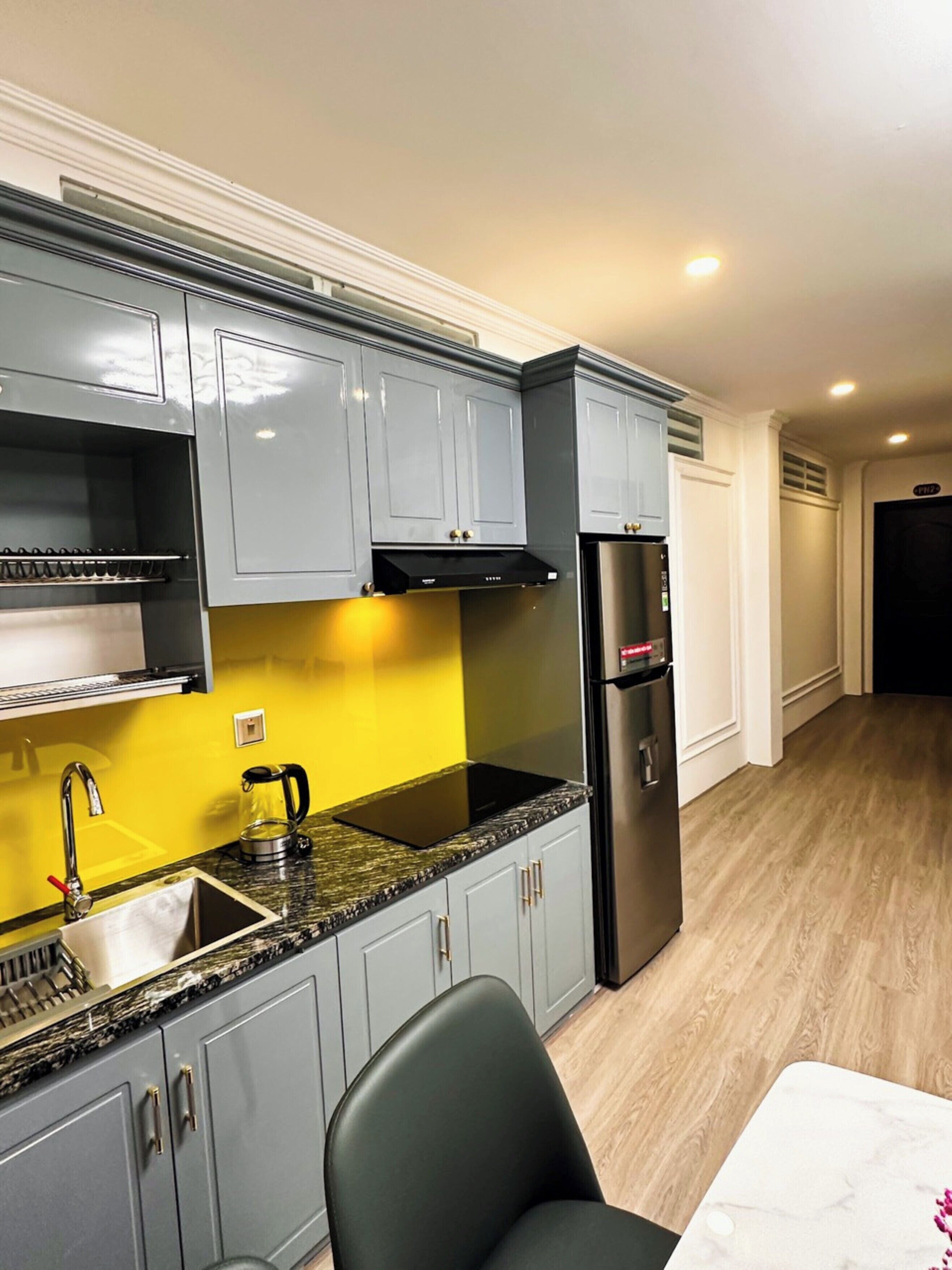 Una cocina compacta con armarios grises, un refrigerador negro y una pared de acento amarilla.