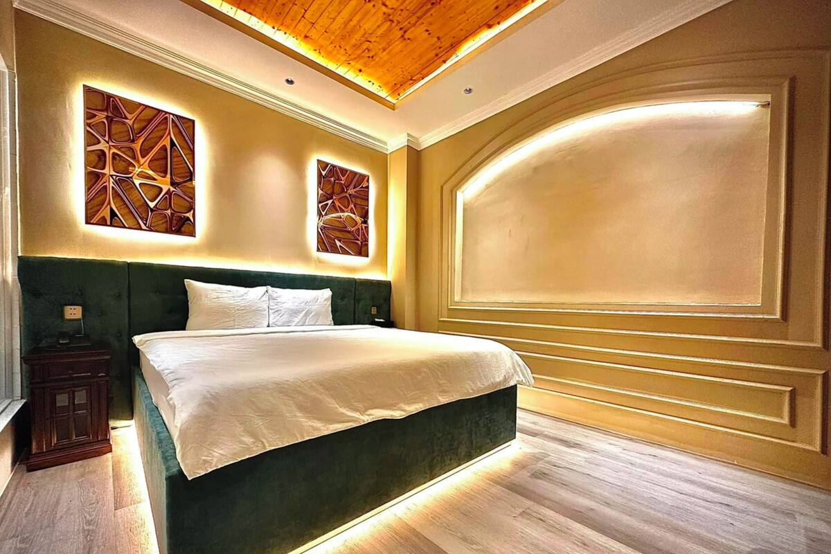 A modern bedroom with a large bed, two wall art pieces, and a wooden ceiling.