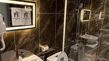 A modern bathroom with a marble wall, a sink, a toilet, and a shower area.