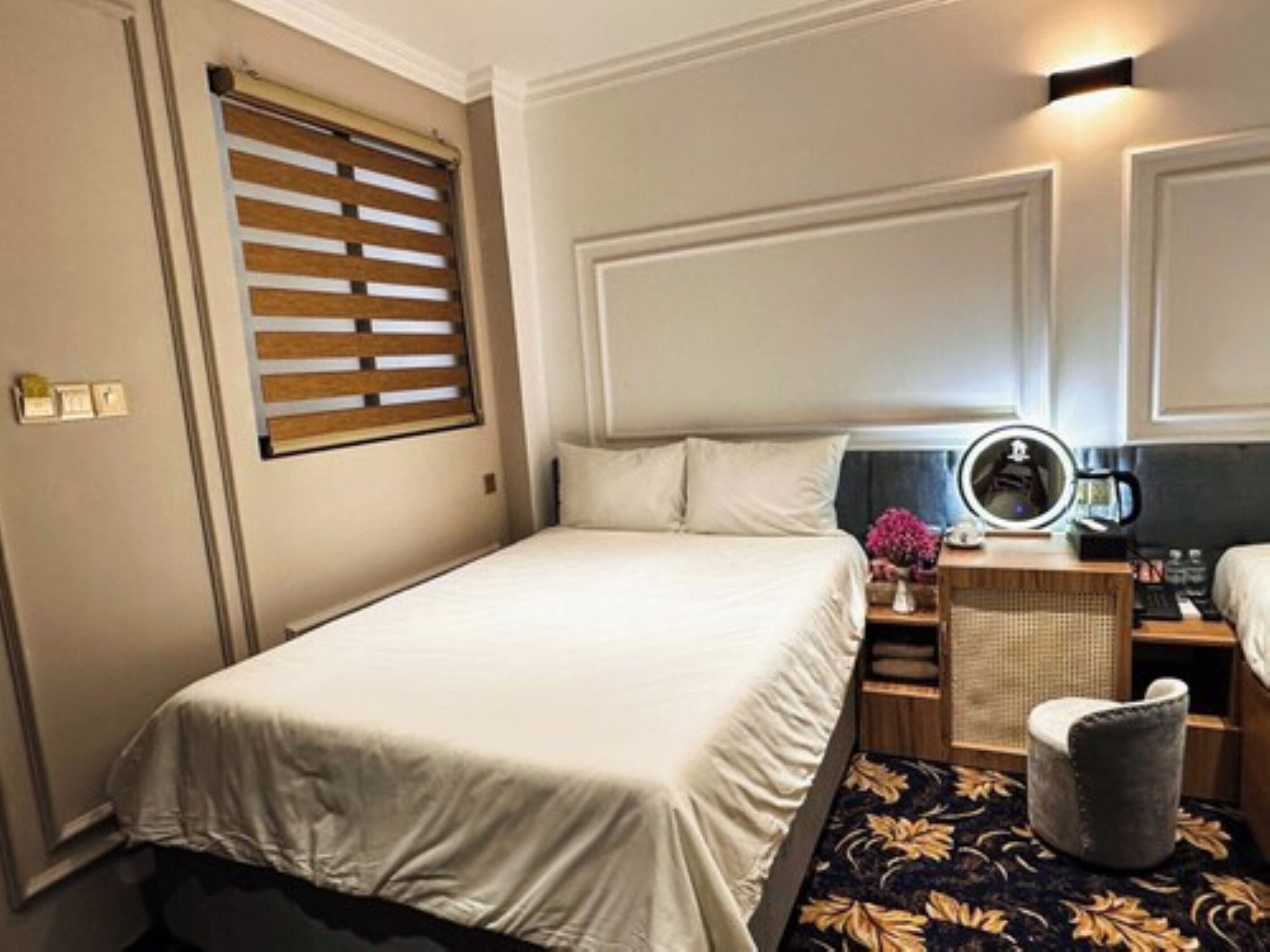 Une chambre d’hôtel bien rangée, avec un lit, une table de chevet, une lampe et une petite chaise.