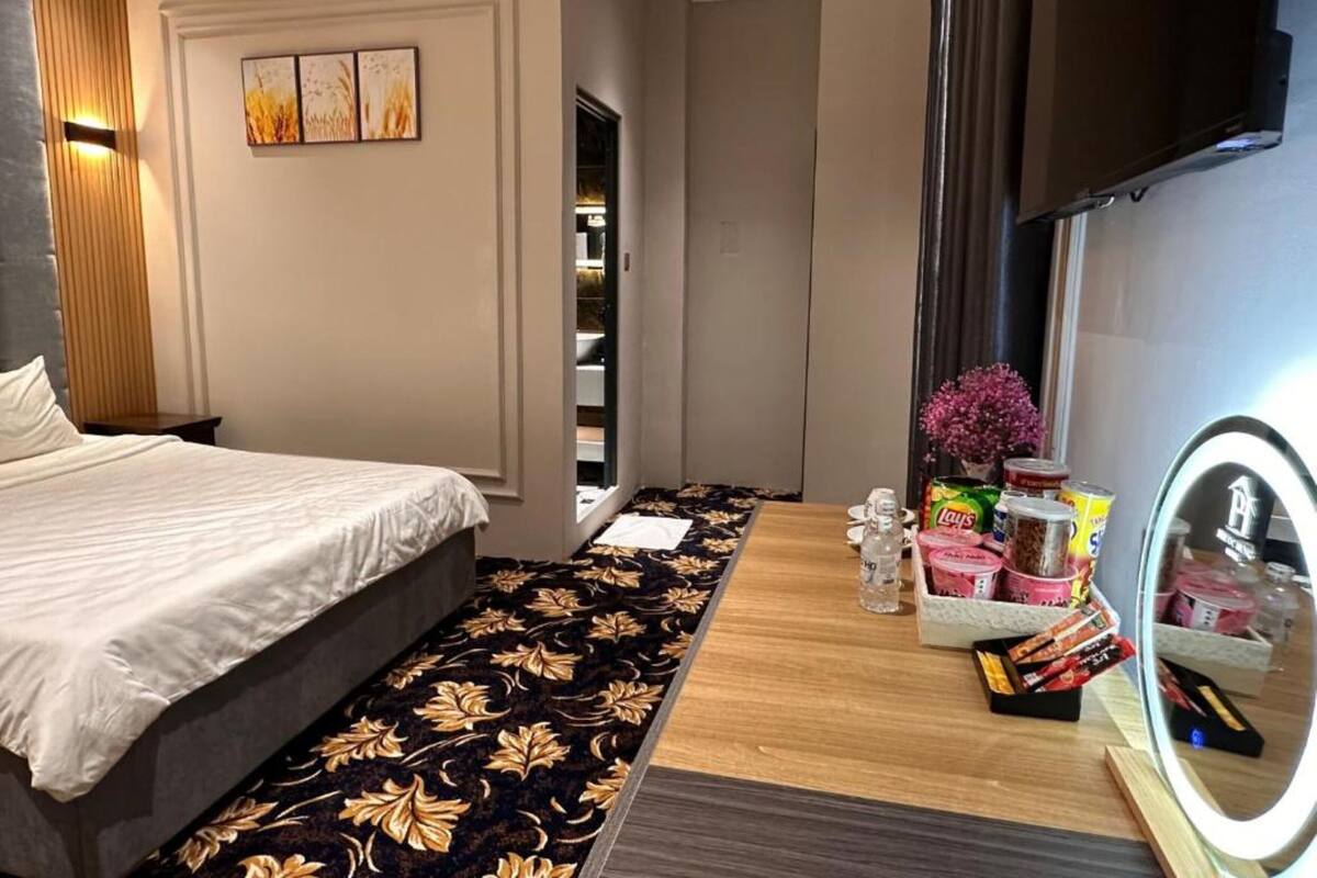 A modern bedroom with a bed, a vanity with a mirror, and a small table with toiletries.