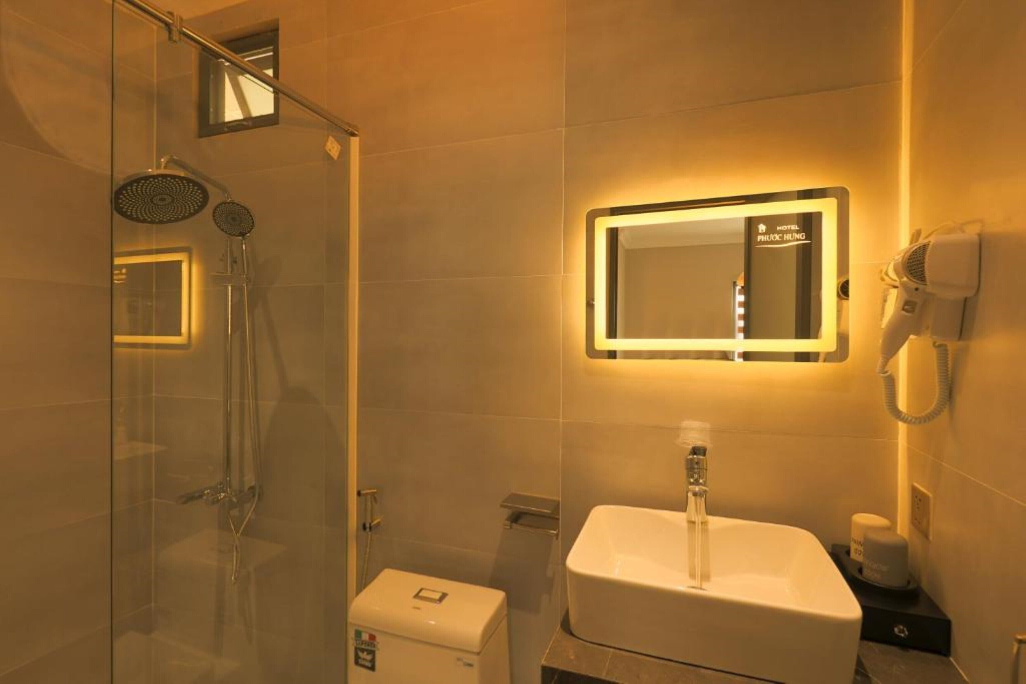 A modern bathroom with a glass-enclosed shower, a white sink, and a mirror with a light above it.