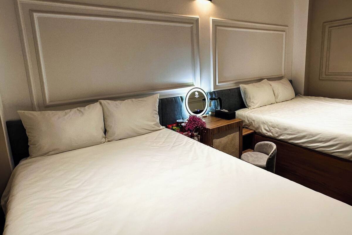 A hotel room with two beds, a bedside table with a lamp, a mirror, and a small chair.