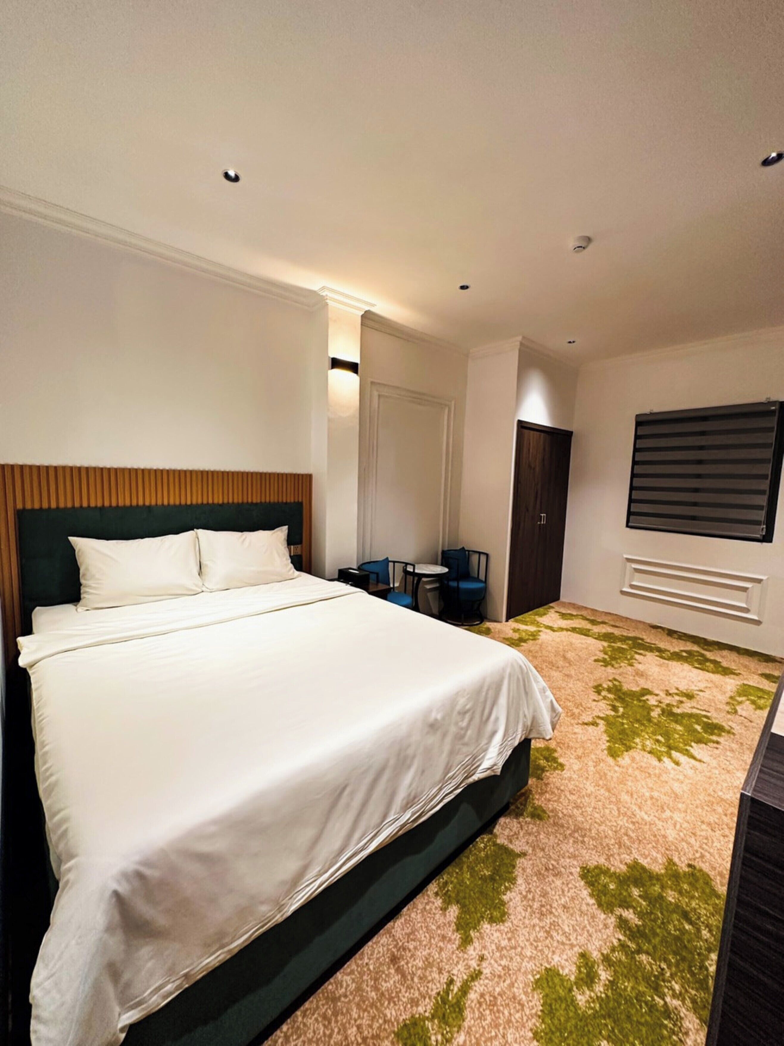 Une chambre d’hôtel avec un grand lit, un bureau, une chaise et une fenêtre avec des stores.