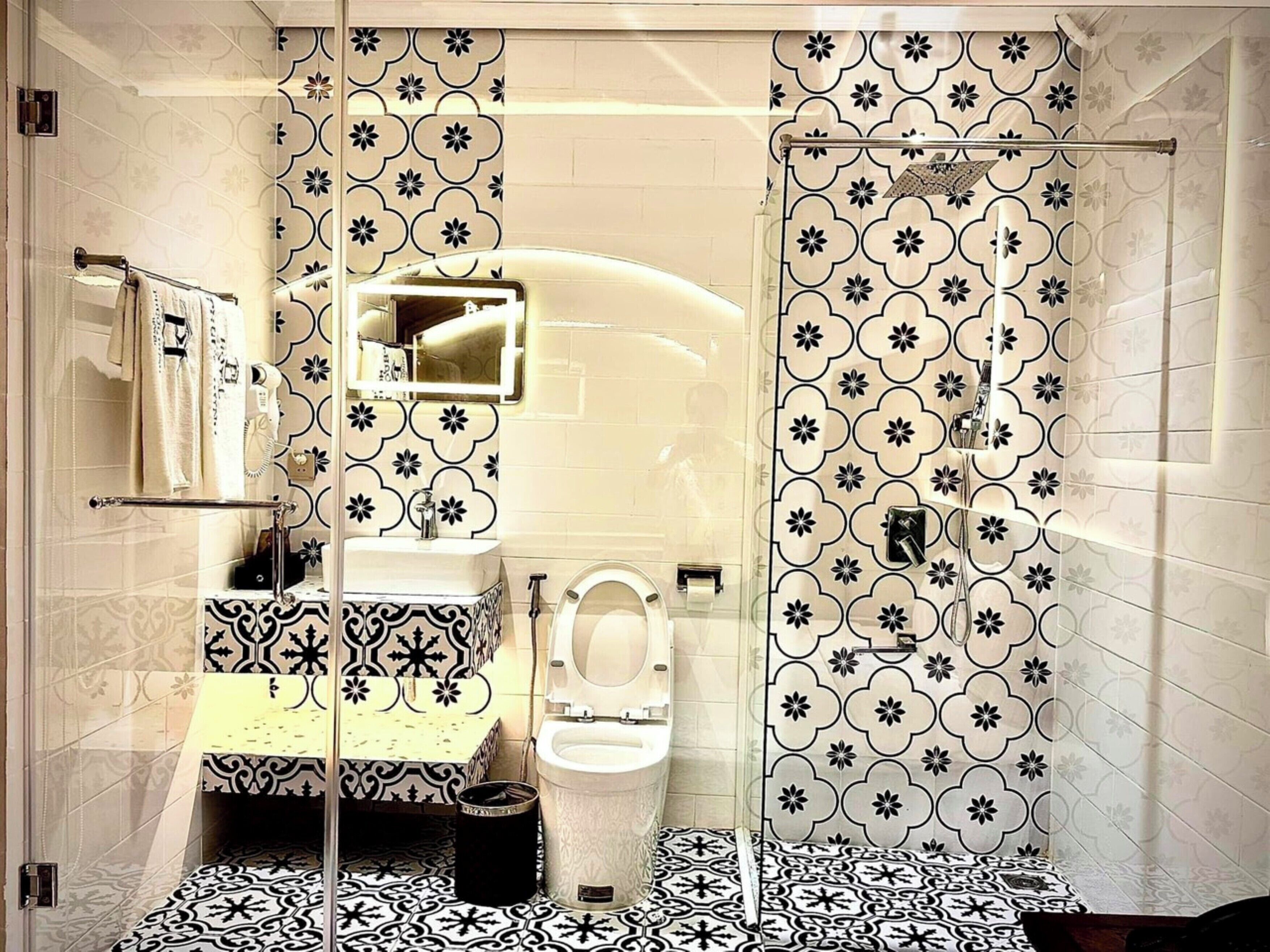 Un baño con ducha, inodoro y lavamanos, con baldosas estampadas en blanco y negro.