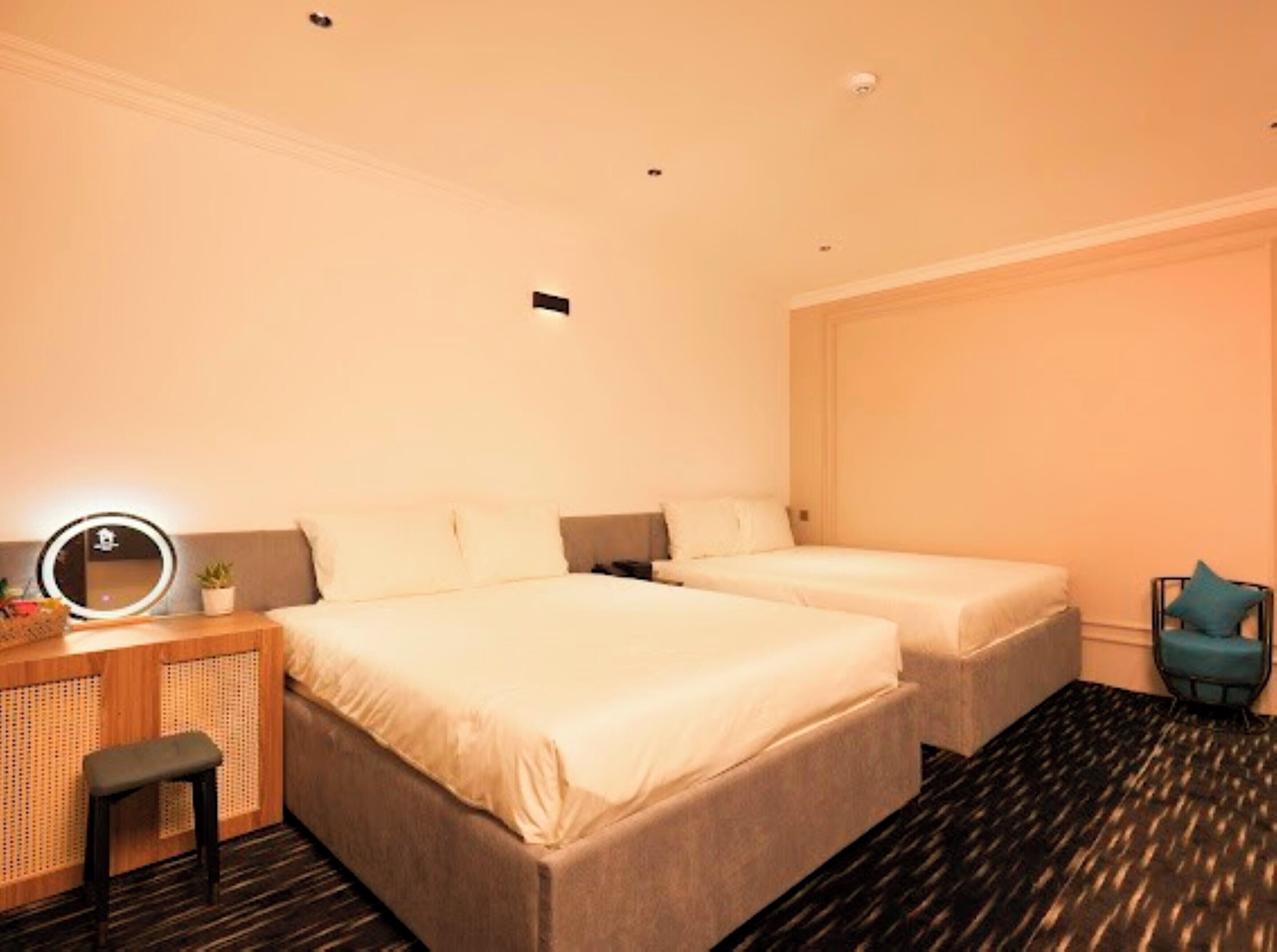A hotel room with two beds, a desk with a mirror, a small stool, and a chair.