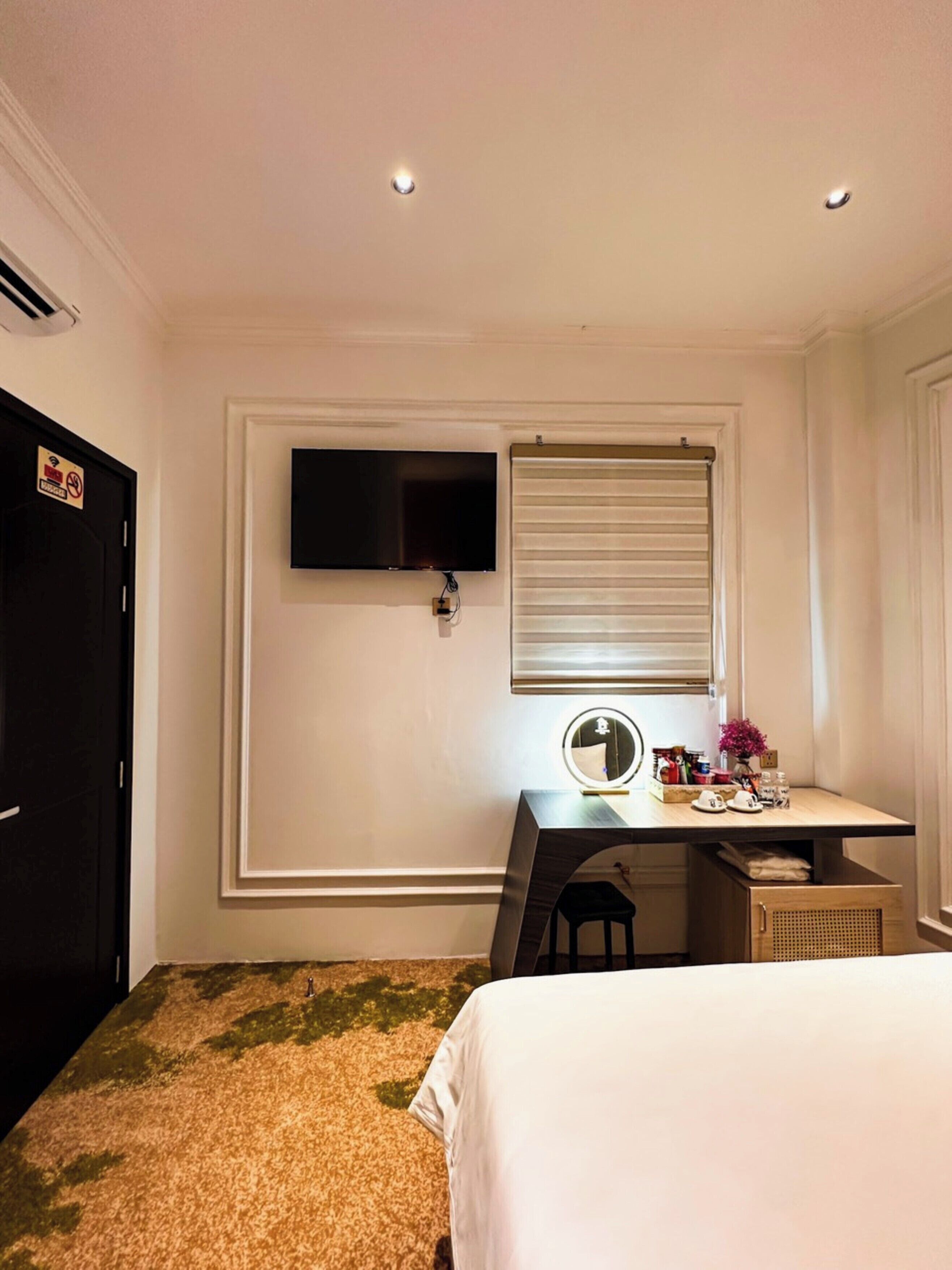 Une chambre à coucher avec un lit, un bureau doté d’un miroir, une télévision et une fenêtre avec des stores.