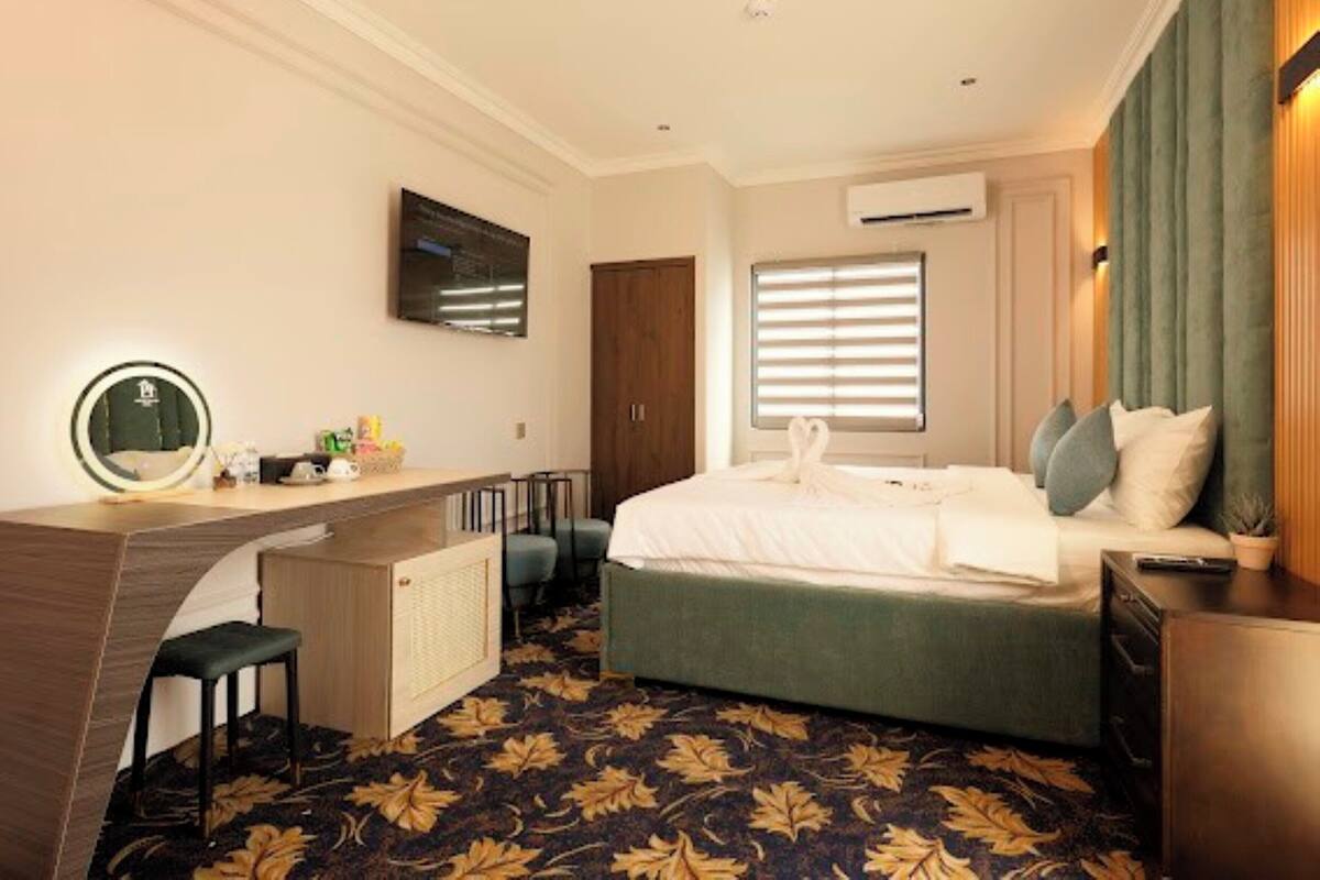 A hotel room with a bed, a desk with a mirror, a TV, and a window with blinds.