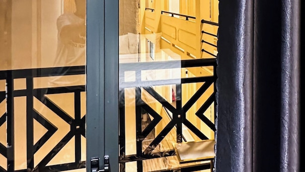 A hotel corridor with a geometric patterned ceiling, a bed with a wooden headboard, and a black metal gate. - Phuoc Hung 3 (Long Chau)