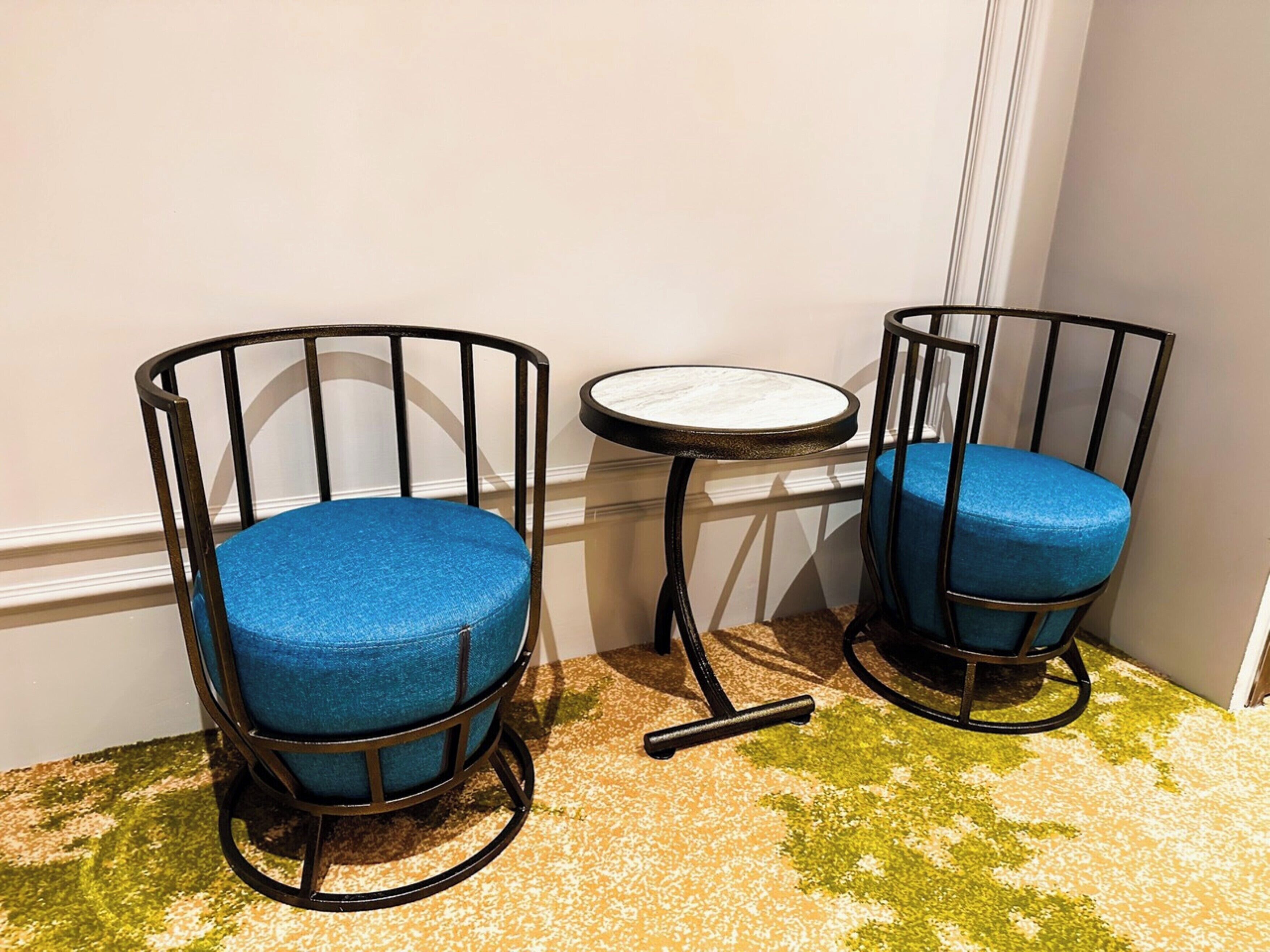 Two blue upholstered chairs with metal frames and a small round table with a marble top.