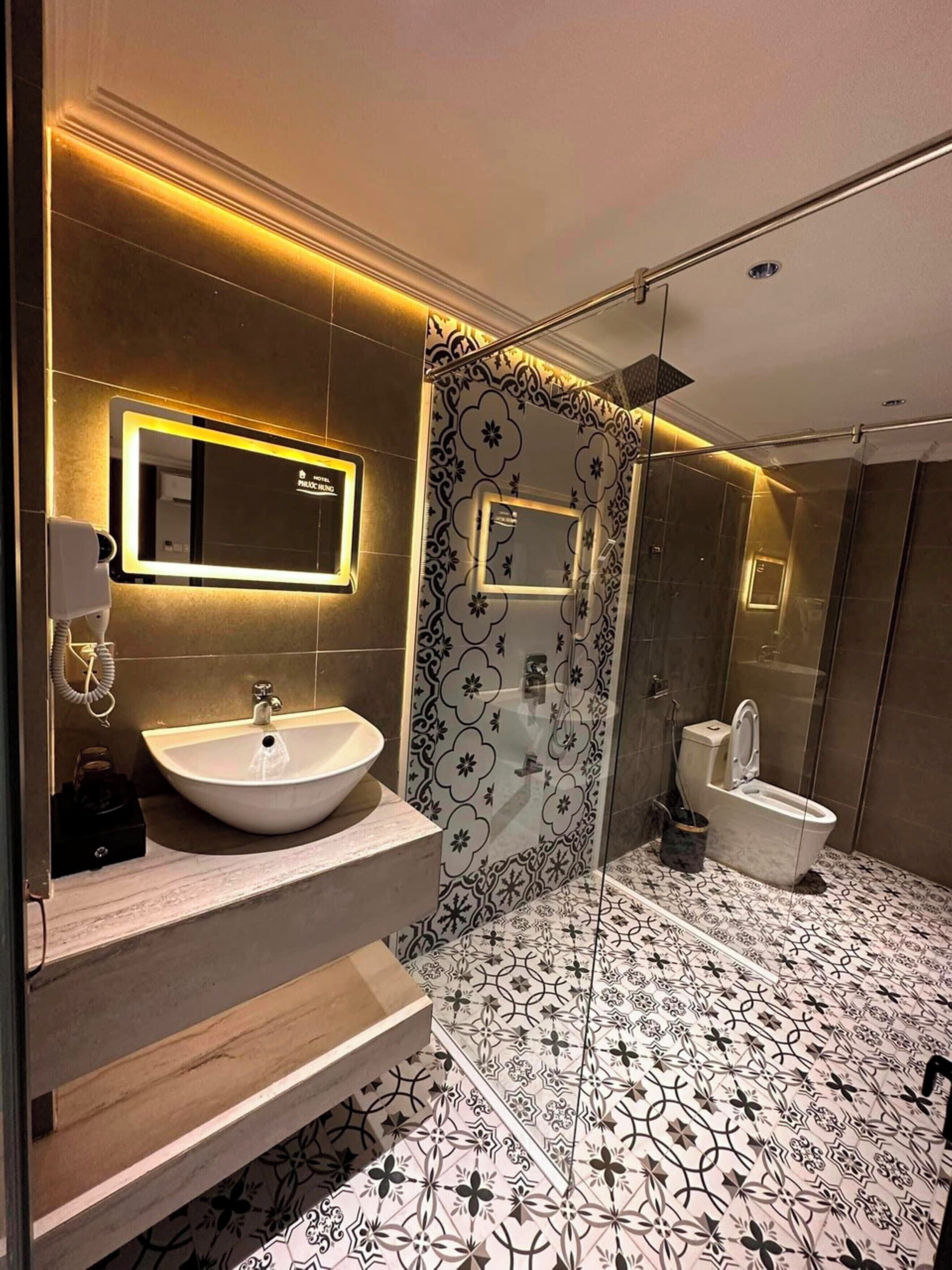 A modern bathroom with a large mirror, two sinks, a toilet, and a shower.