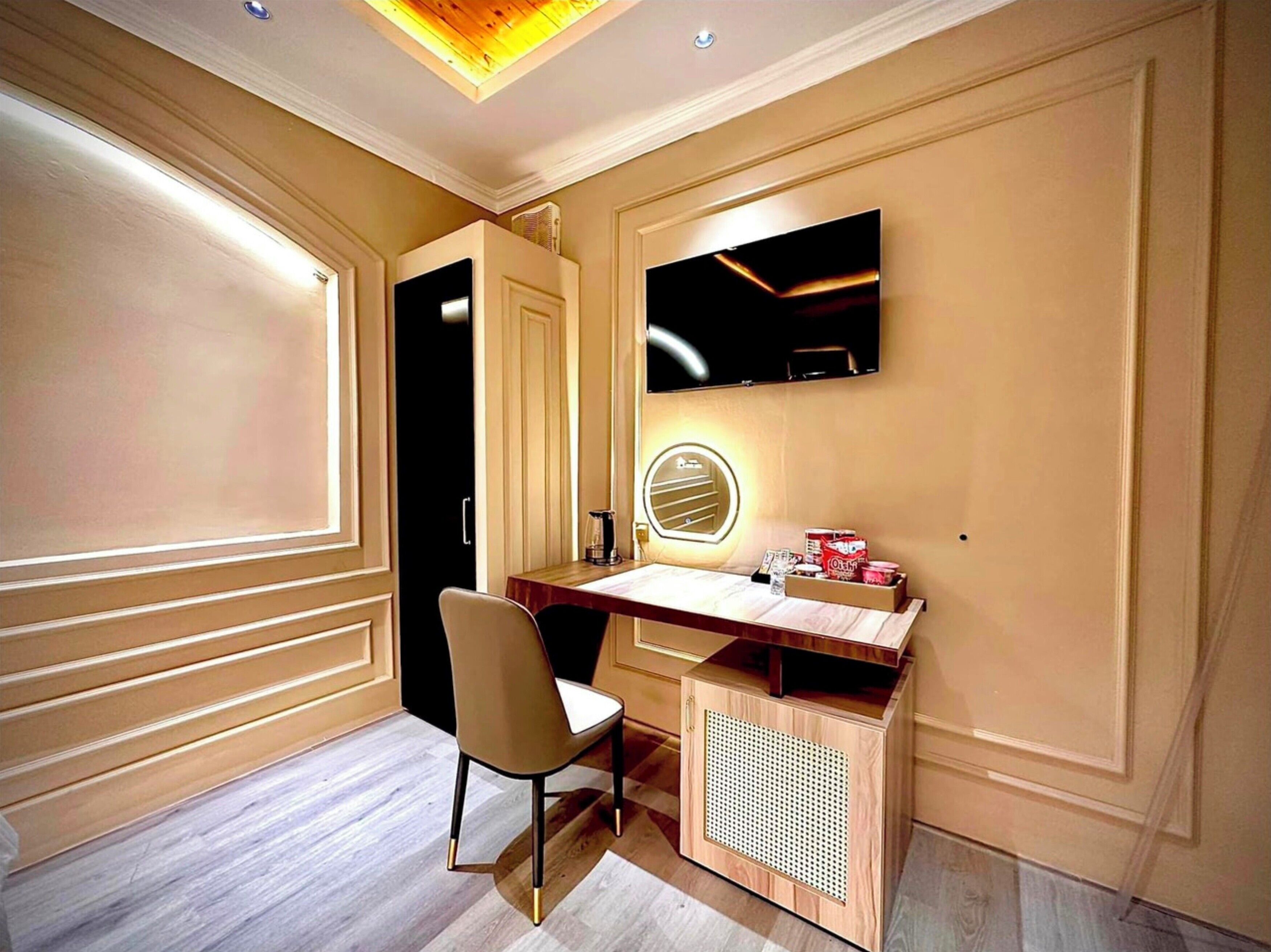 Una habitación con escritorio de madera, una silla, televisor montado en la pared y una puerta.