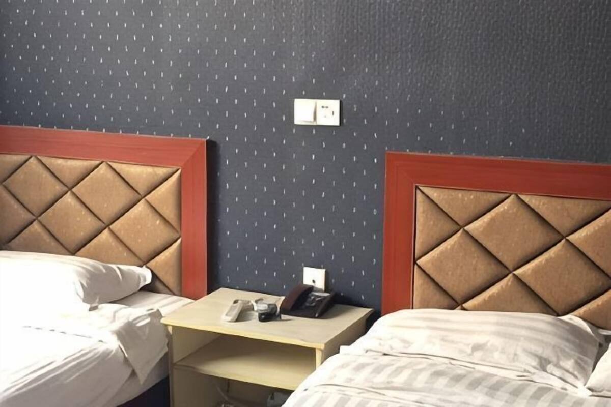 A hotel room with two beds, a nightstand, and a wall socket.