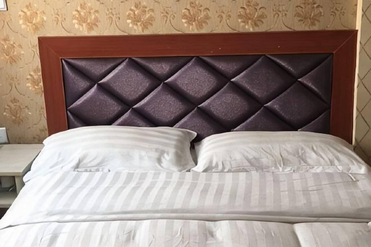 A bed with a tufted headboard, white bedding, and a floral wallpaper pattern.