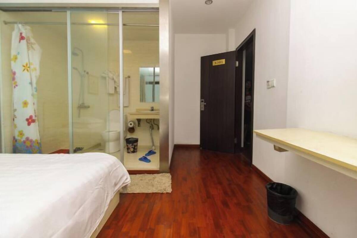 A bedroom with a bed, a shower, a bathroom, and a door with a sign.