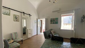 Ein geräumiges Wohnzimmer mit großem Fenster, einem Essbereich mit gemusterten Stühlen und einer Wand mit Spiegel.