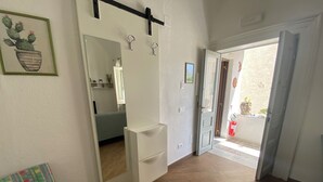 Ein Zimmer mit Bett, Stuhl, Spiegel und einer Tür zu einem Außenbereich mit Feuerlöscher.
