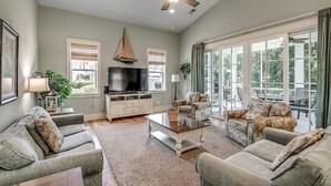 A spacious living room with a ceiling fan, large windows, a flat-screen TV, and a cozy seating area with two sofas and a coffee table.