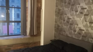 A bedroom with a bed, a window, and a geometric-patterned wall. - 1 Bed Flat - Sleeps 2 - Parking - Wifi (Bradford)