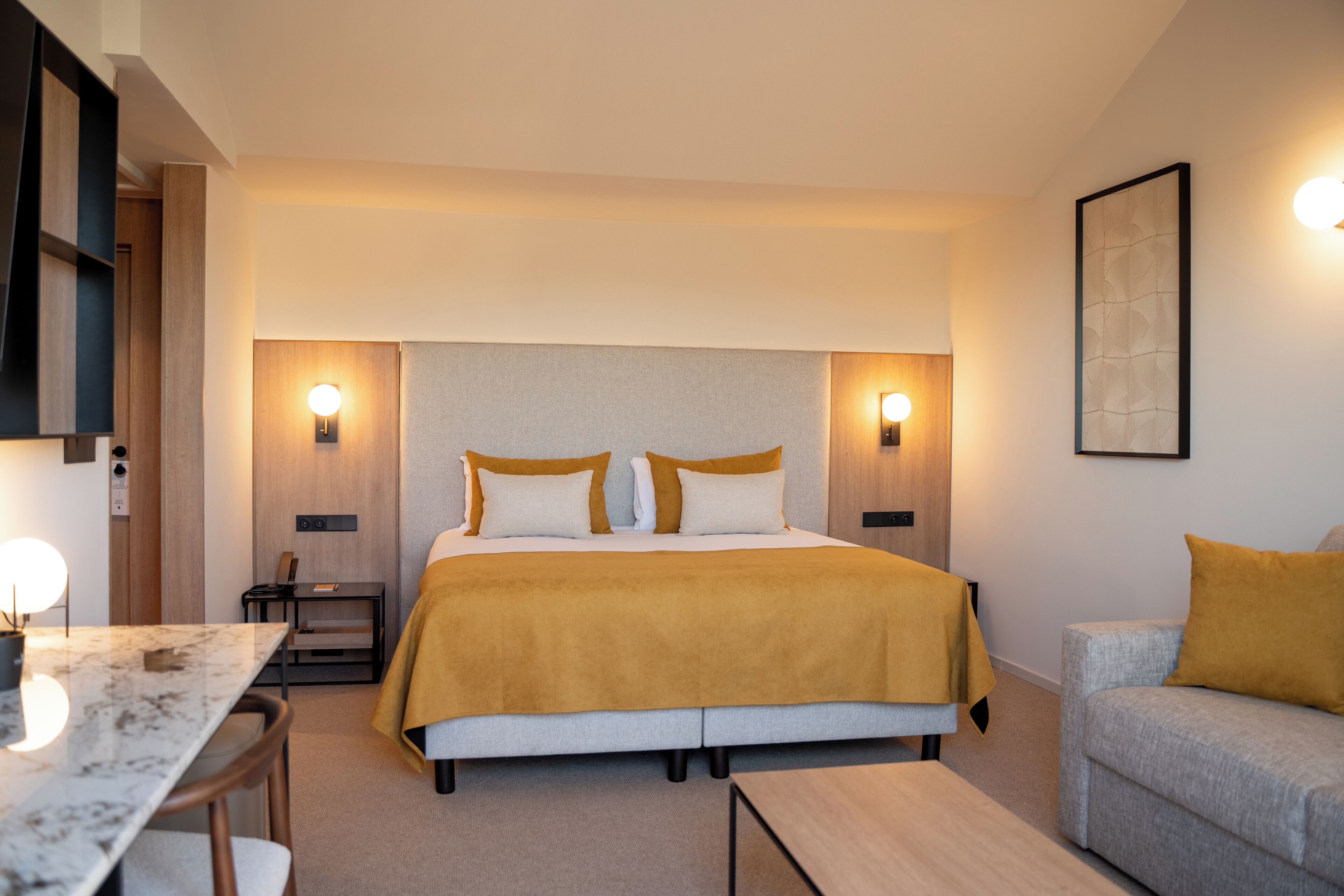 A modern hotel room with a large bed, bedside tables, a desk, and a sofa.